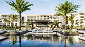 A hotel with a pool area, palm trees, and a covered seating area.