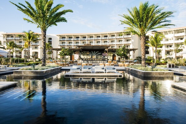 Un hotel con zona de piscina, palmeras y un área de estar cubierta.