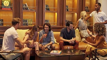A group of people seated on a leather couch in a warmly lit room with wooden bookshelves filled with books.