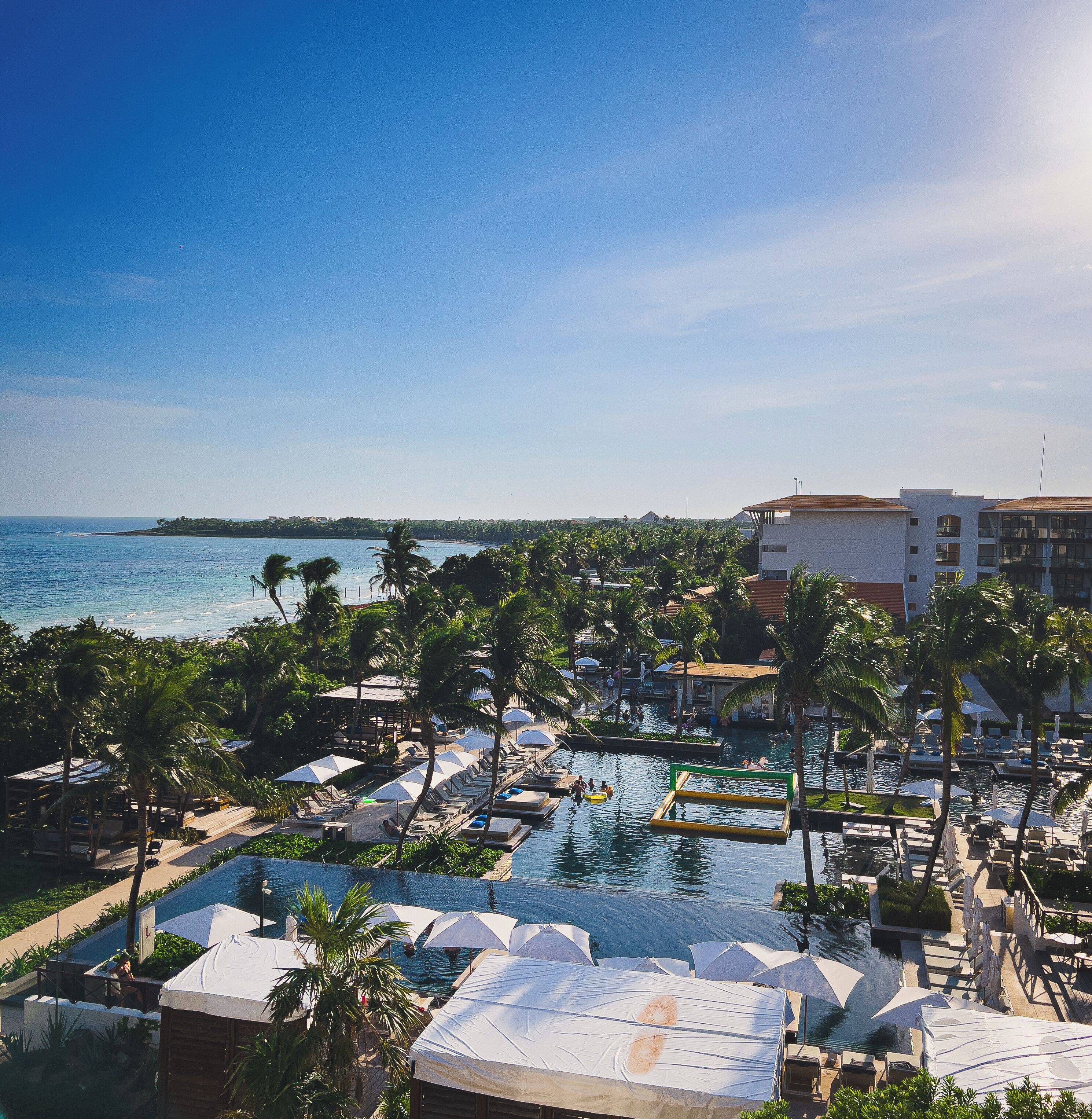 A resort with a pool area, palm trees, and a view of the sea.