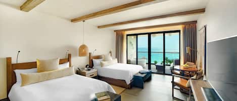 A hotel room with two beds, a desk, a TV, and a balcony with a view of the sea.