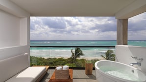 A modern bathroom with a bathtub, a wooden bench, and a view of the ocean.