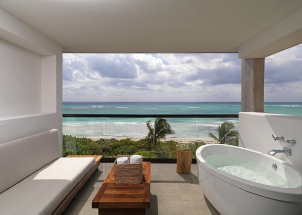 A modern bathroom with a bathtub, a wooden bench, and a view of the ocean.