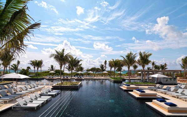 A pool area with lounge chairs and umbrellas, surrounded by palm trees and a clear sky. - Unico Hotel Riviera Maya - Adults Only - All Inclusive (Kantenah)