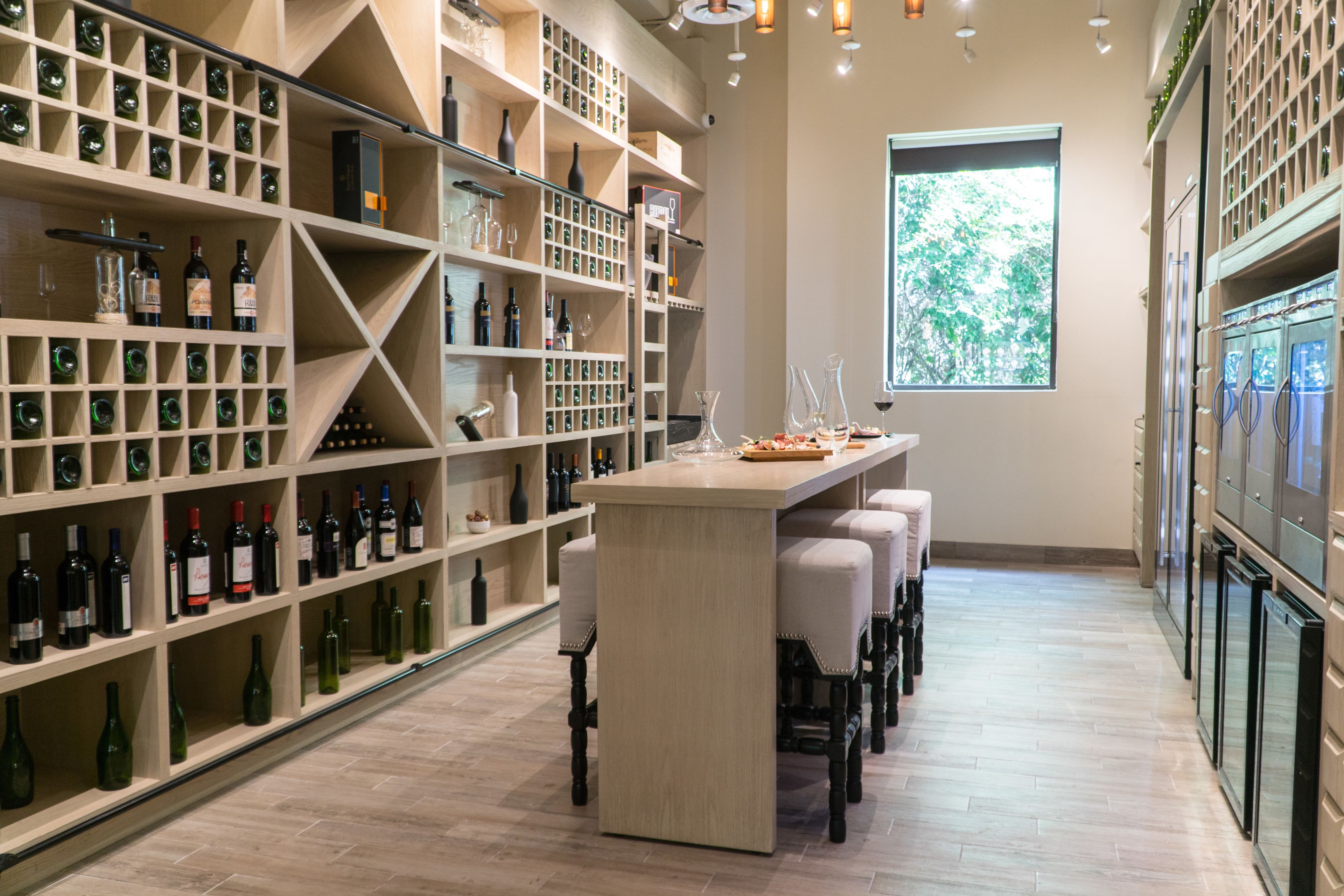 A wine cellar with shelves of wine bottles, a tasting table, and a large window.