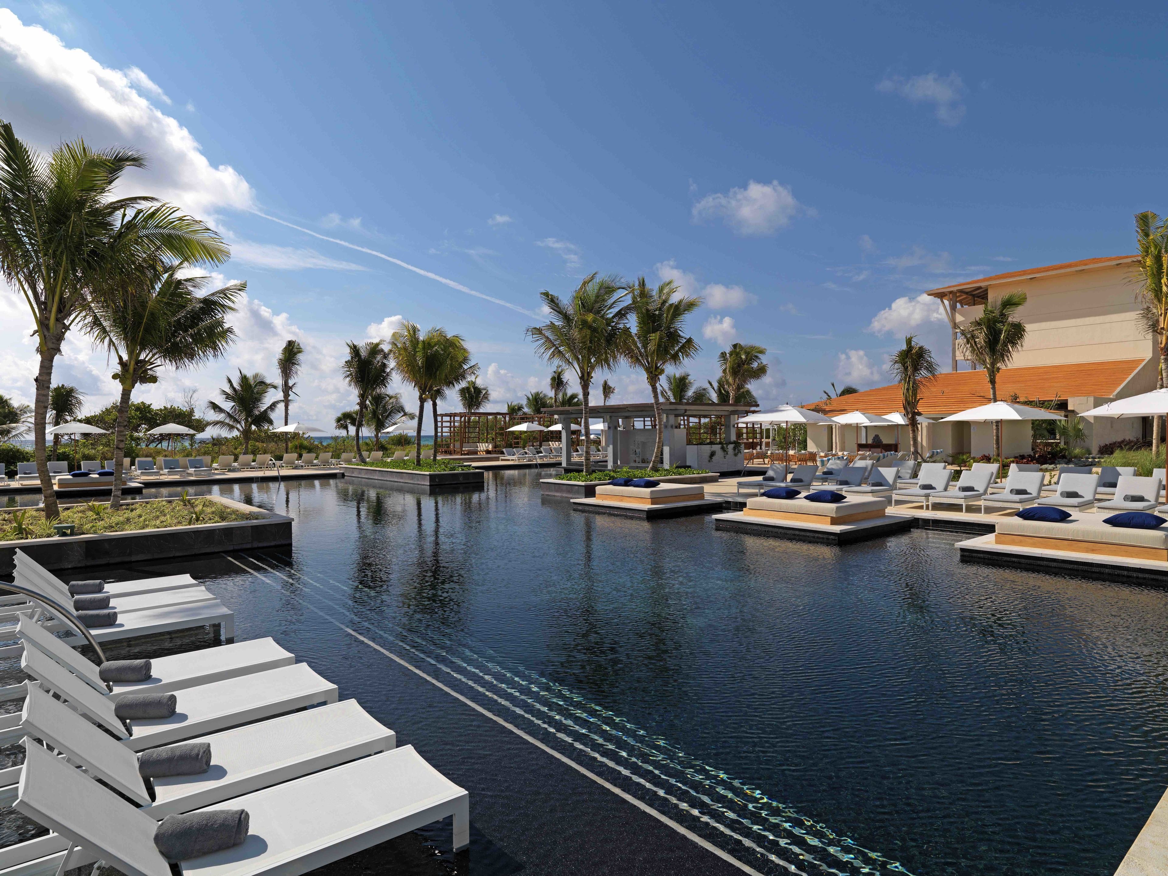 A resort pool area with lounge chairs, palm trees, and a clear sky.