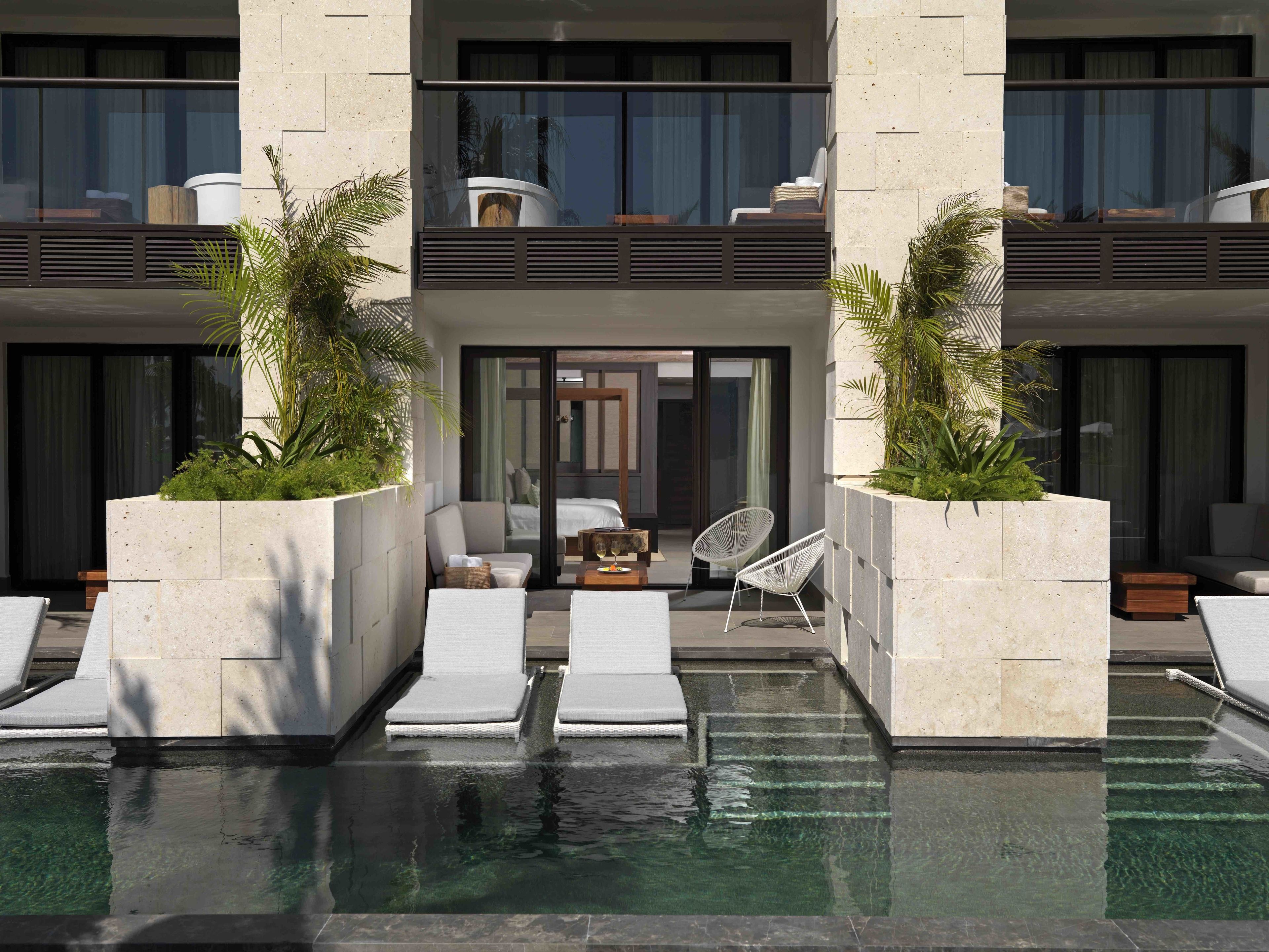 Un hotel moderno con piscina, sillas de descanso y un área de estar con mesa y sillas.