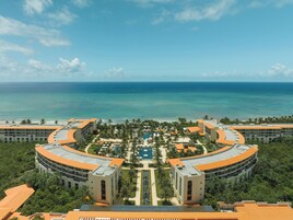 Un resort con piscina central, rodeado de palmeras y una playa.