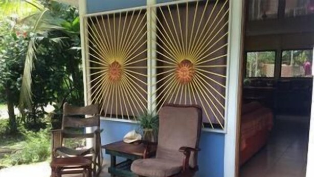 A room with two wooden chairs and a table, a window with a sunburst design, and a view of the outdoors. - La Casita del Sol (Cahuita)