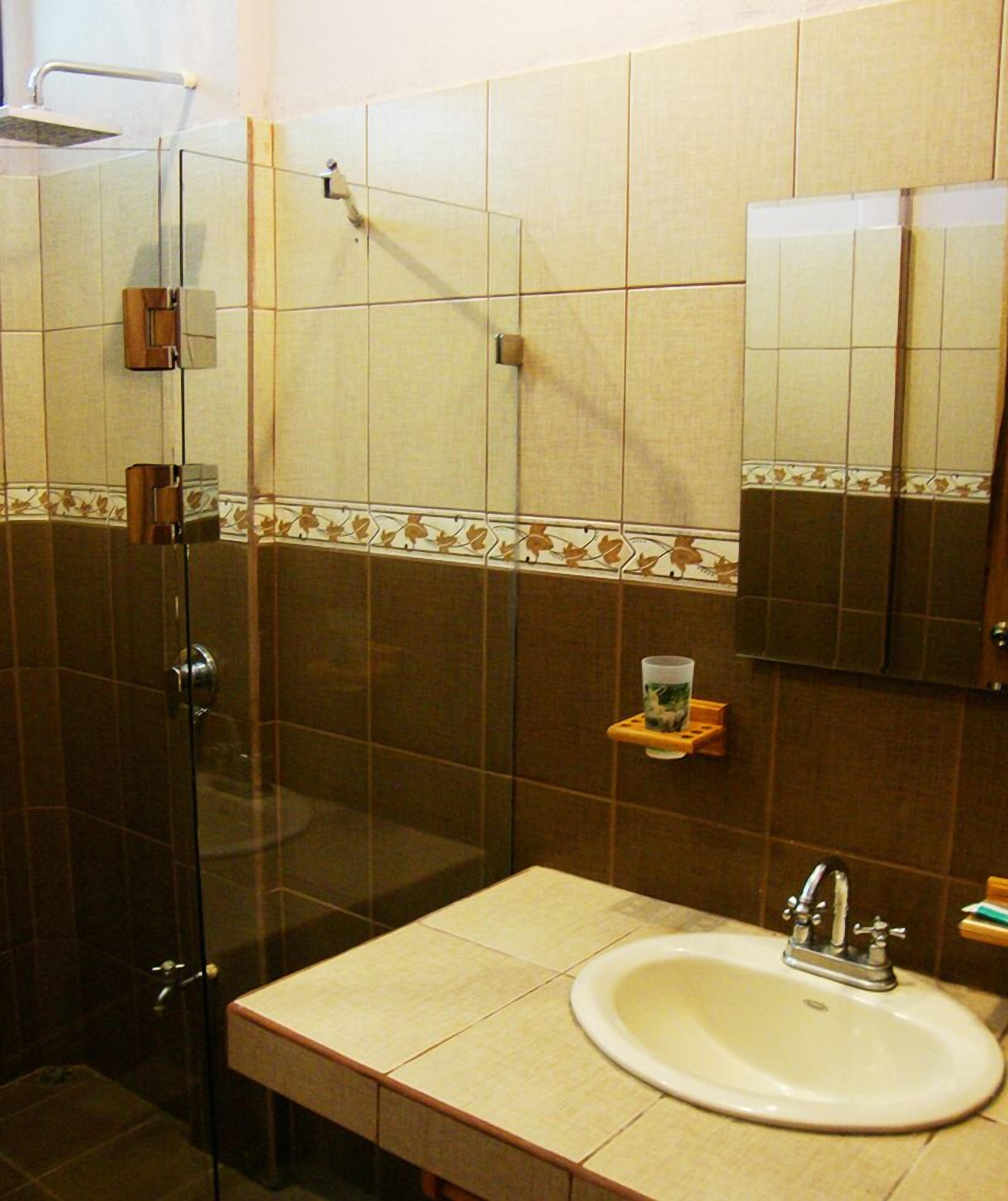 A bathroom with a glass shower enclosure, a sink with a mirror, and a small shelf with toiletries.