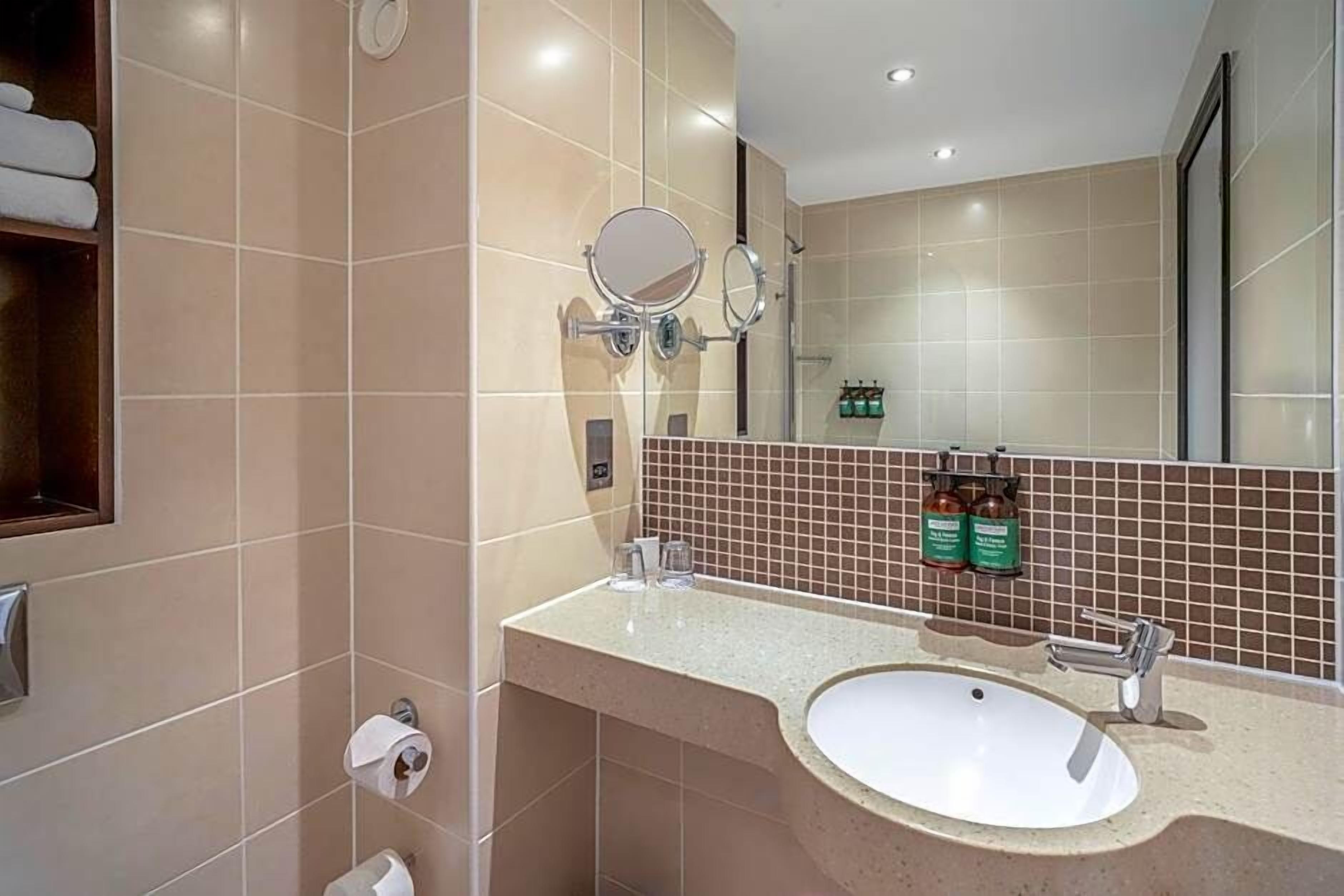 A modern bathroom with a large mirror, a sink, and a towel rack.