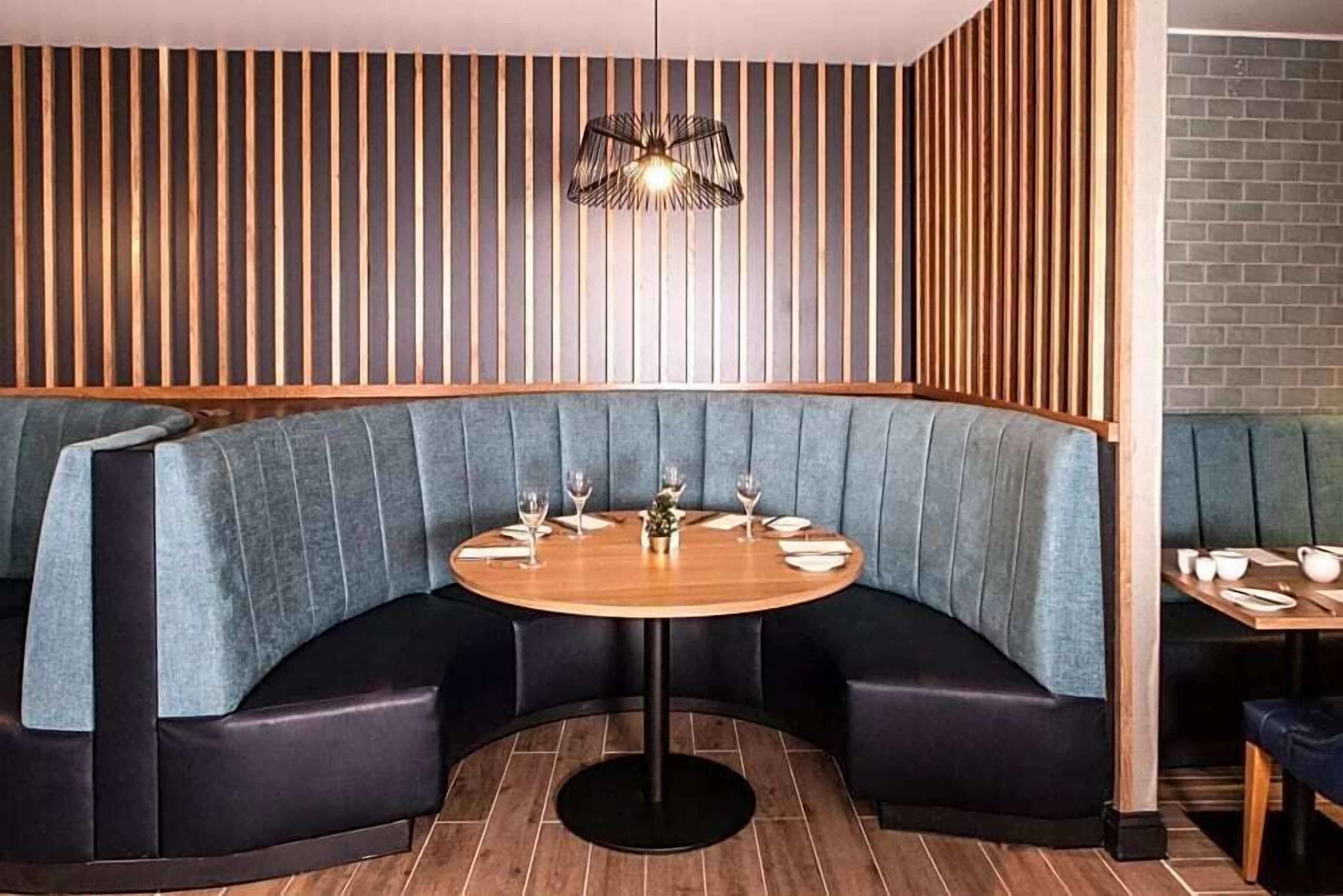 Un restaurant doté d’un espace salon aux lignes courbes, d’une table ronde et d’un mur en lambris de bois.