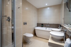 Un baño moderno con ducha envuelta en vidrio, inodoro y bañera independiente con dos lavamanos.