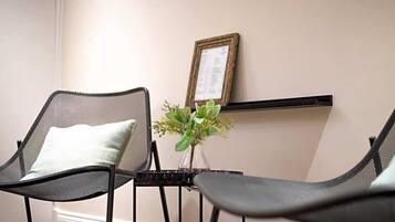 Una habitación con dos sillas de malla negra, una con cojín blanco, y una pequeña mesa con un florero de plantas verdes.