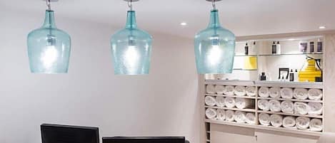 A modern interior with three hanging blue glass pendant lights, a white wall with a shelf of neatly rolled towels, and a black table with two chairs.