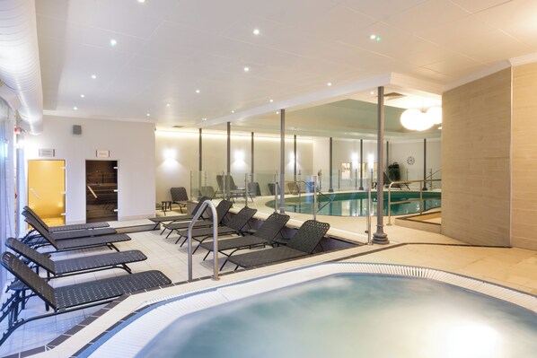 Un área de piscina interior moderna con sillones de descanso y una pared de vidrio.