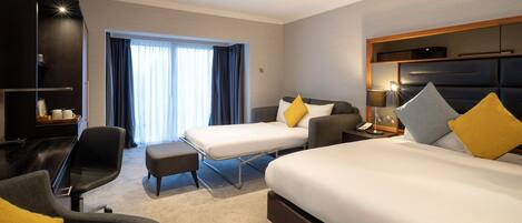 Een hotelkamer met twee bedden, een bureau, een stoel, een bank en een groot raam met gordijnen.