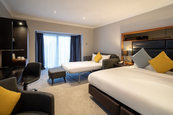 Habitación de hotel con dos camas, un escritorio, una silla, un sofá y un ventanal con cortinas.