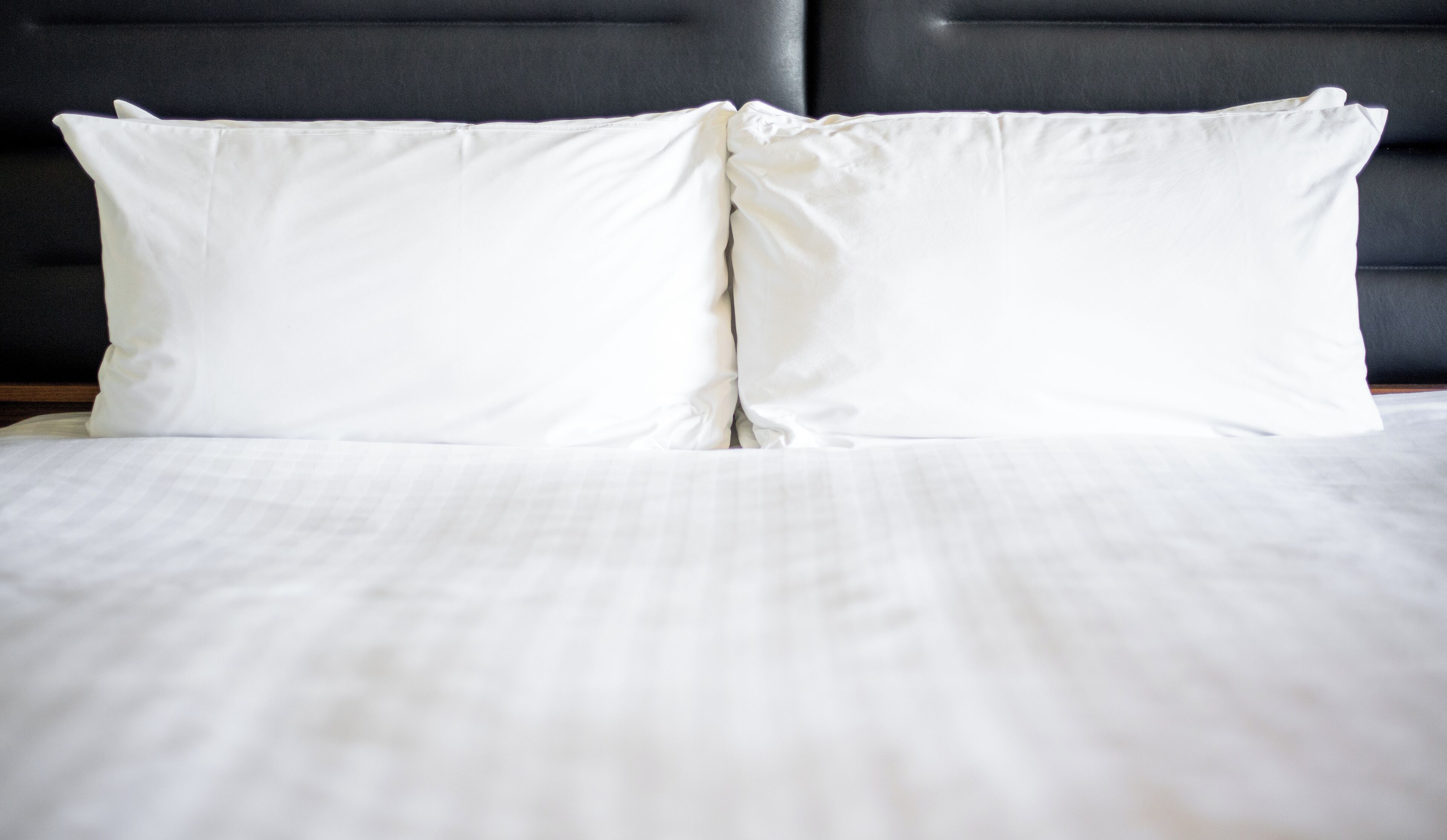 A neatly made bed with white linens and pillows, a dark headboard, and a wooden nightstand.