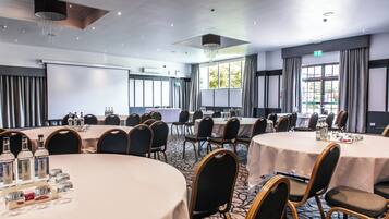 A conference room with multiple round tables, chairs, and a projector screen.