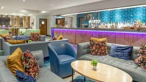 A modern lobby with grey sofas, a blue armchair, and a bar area with a blue geometric wall and a purple neon light. - Felbridge Gatwick Hotel & Spa (East Grinstead)
