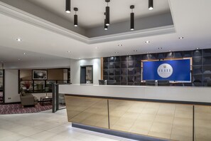 Zona de recepción moderna de un hotel con un letrero azul que dice "ELITE" y un mostrador de recepción.