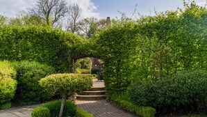 A paved pathway leading through a lush garden with a brick building in the background. - Felbridge Gatwick Hotel & Spa (East Grinstead)