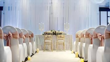Une allée de cérémonie de mariage avec des chaises blanches et une table décorée de fleurs et de bougies.