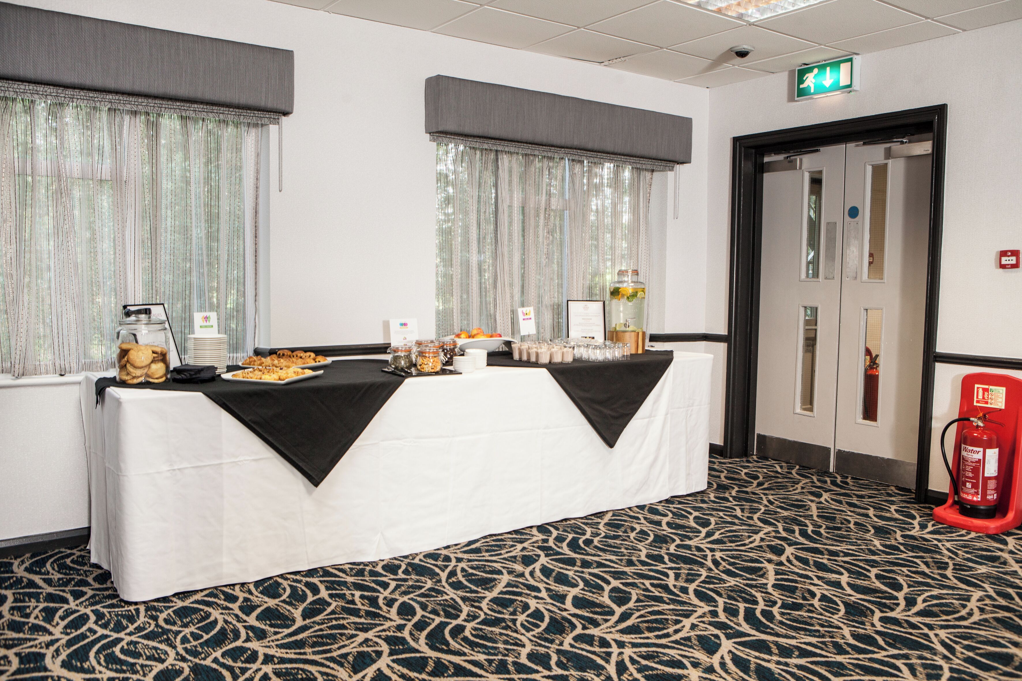 A conference room with a table set for a meeting, a fire extinguisher, and a door with an exit sign.
