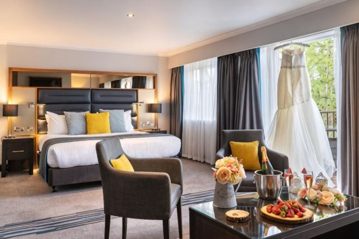 A hotel room with a bed, a desk with a vase of flowers, a chair, and a view of a balcony.