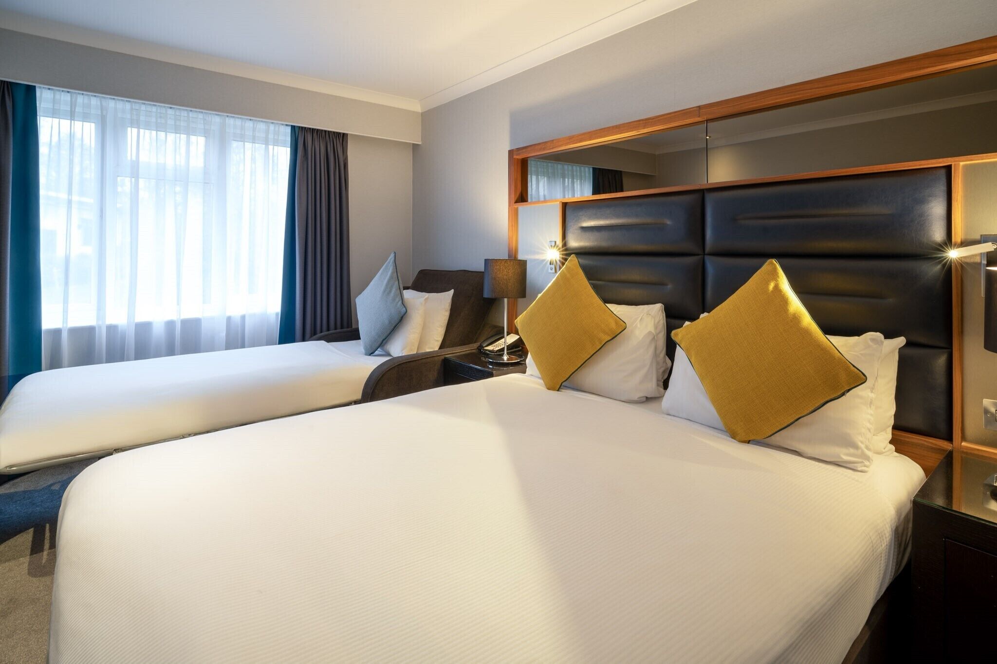 Hotellihuone, jossa on kaksi sänkyä, suuri peili ja yöpöytä, jossa on lamppu.
