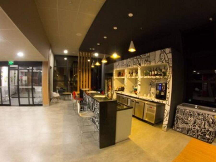A modern bar area with a counter, shelves with bottles, and a seating area with chairs.