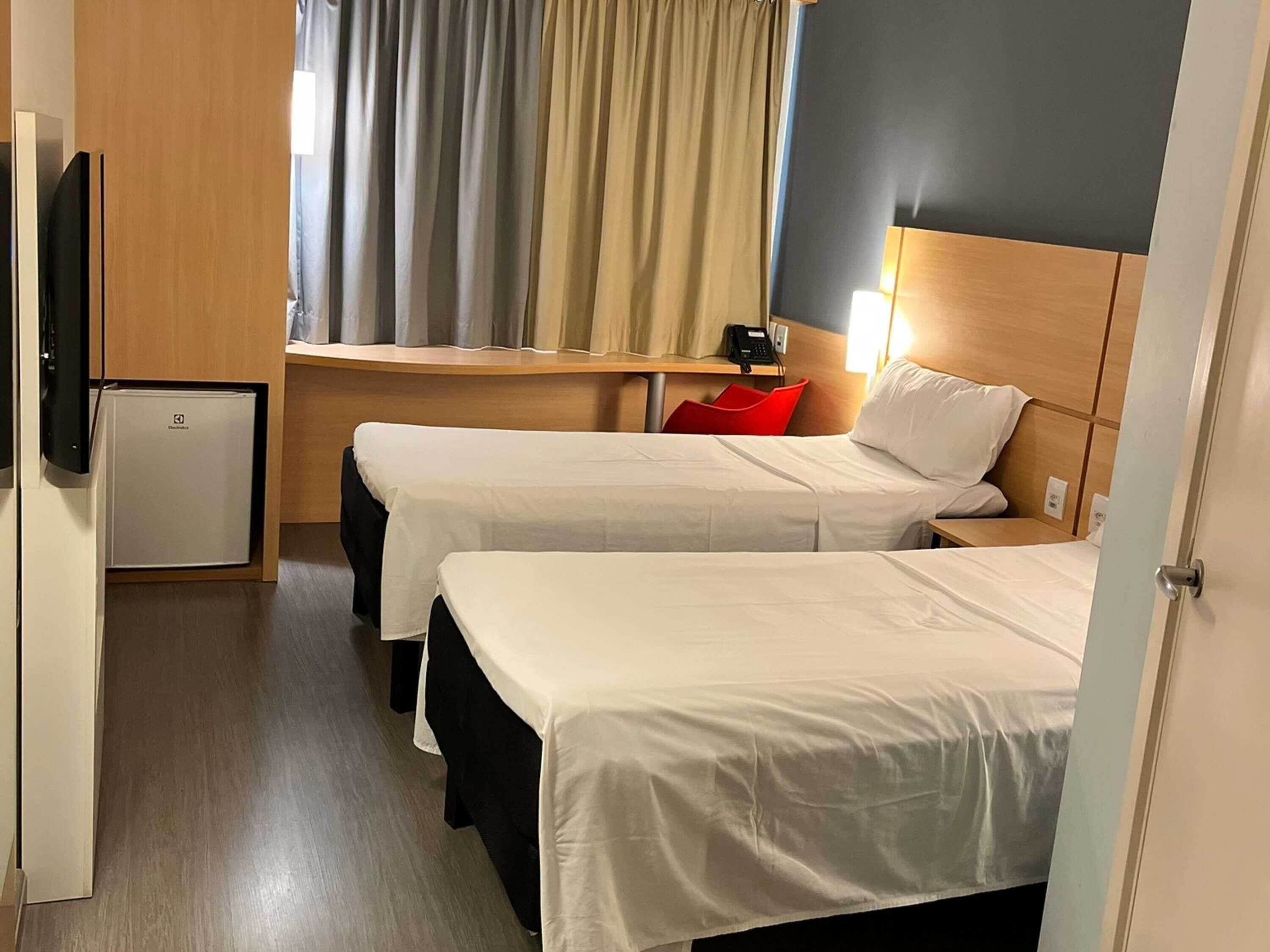 Una habitación de hotel con dos camas, un escritorio, un refrigerador pequeño y una televisión.