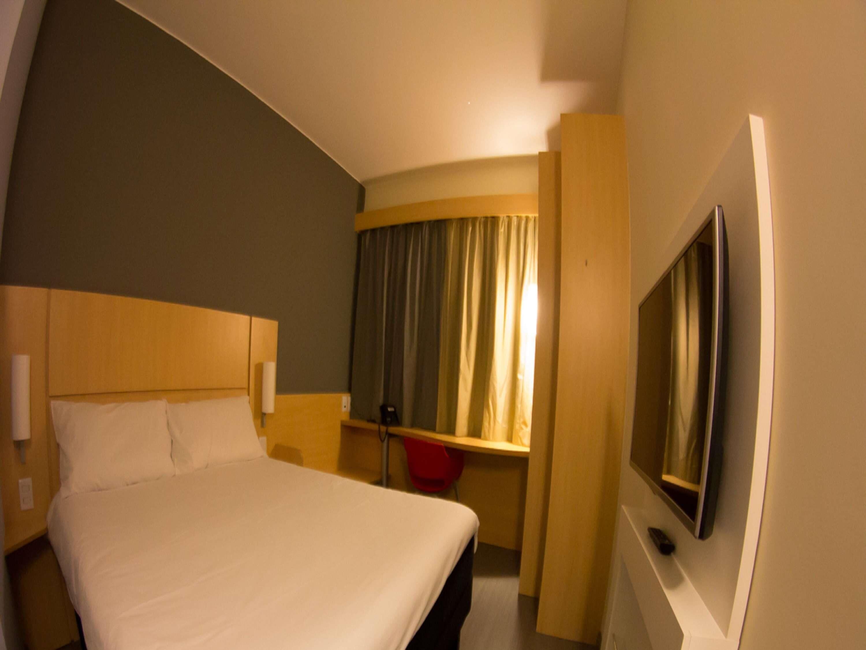 A hotel room with a bed, a desk, a chair, a TV, and curtains.