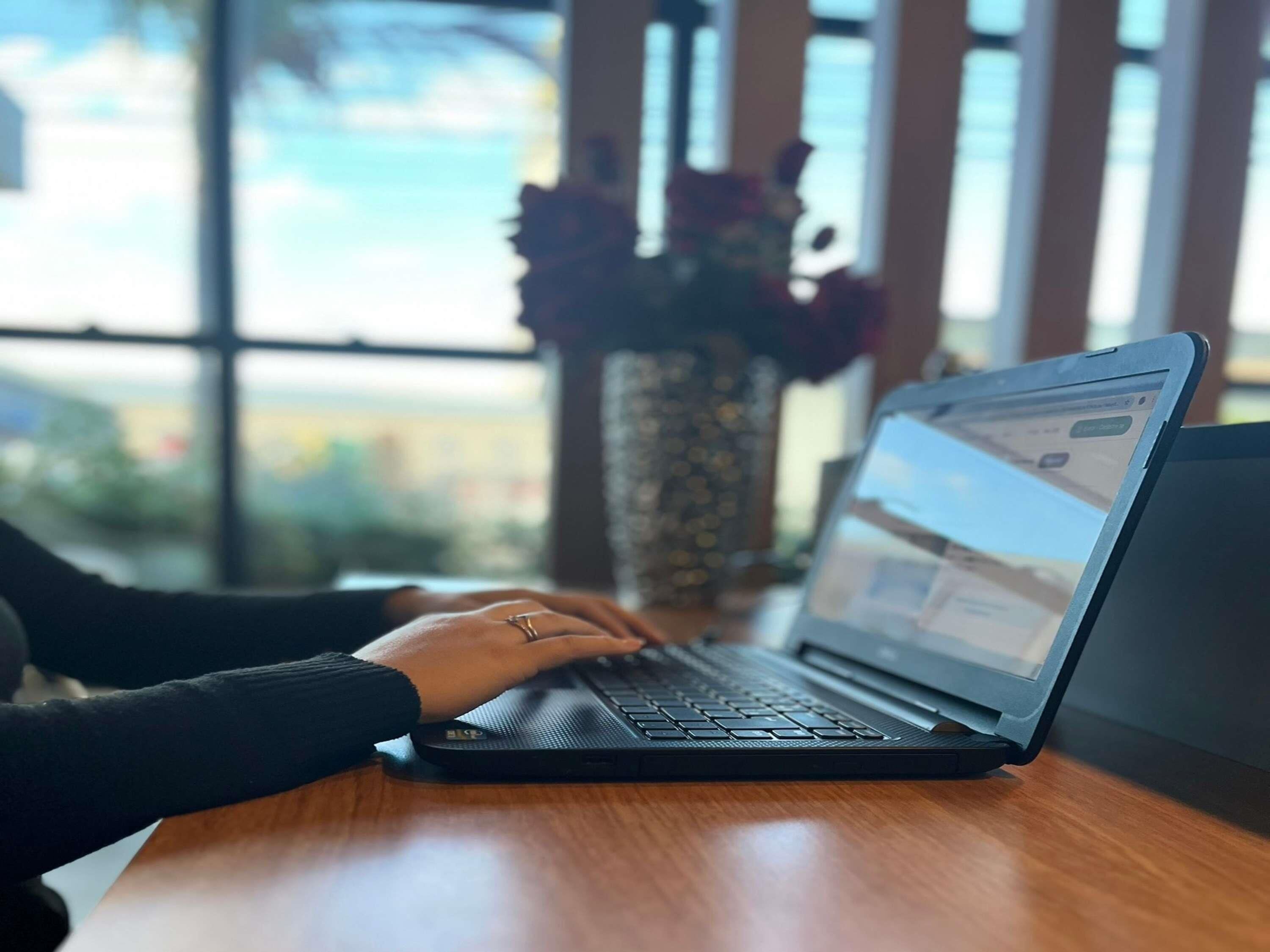 Een laptop op een houten bureau, met een raam op de achtergrond.