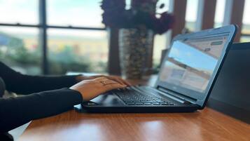 Een laptop op een houten bureau, met een raam op de achtergrond.
