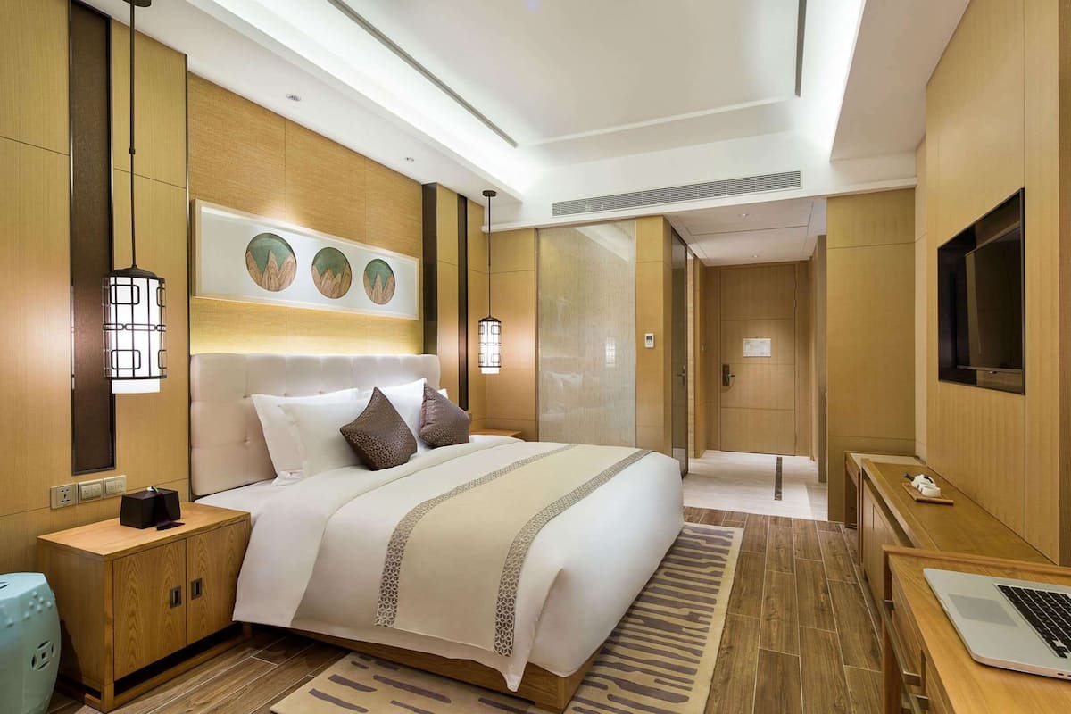 A modern hotel room with a large bed, bedside tables, a desk, and a television.