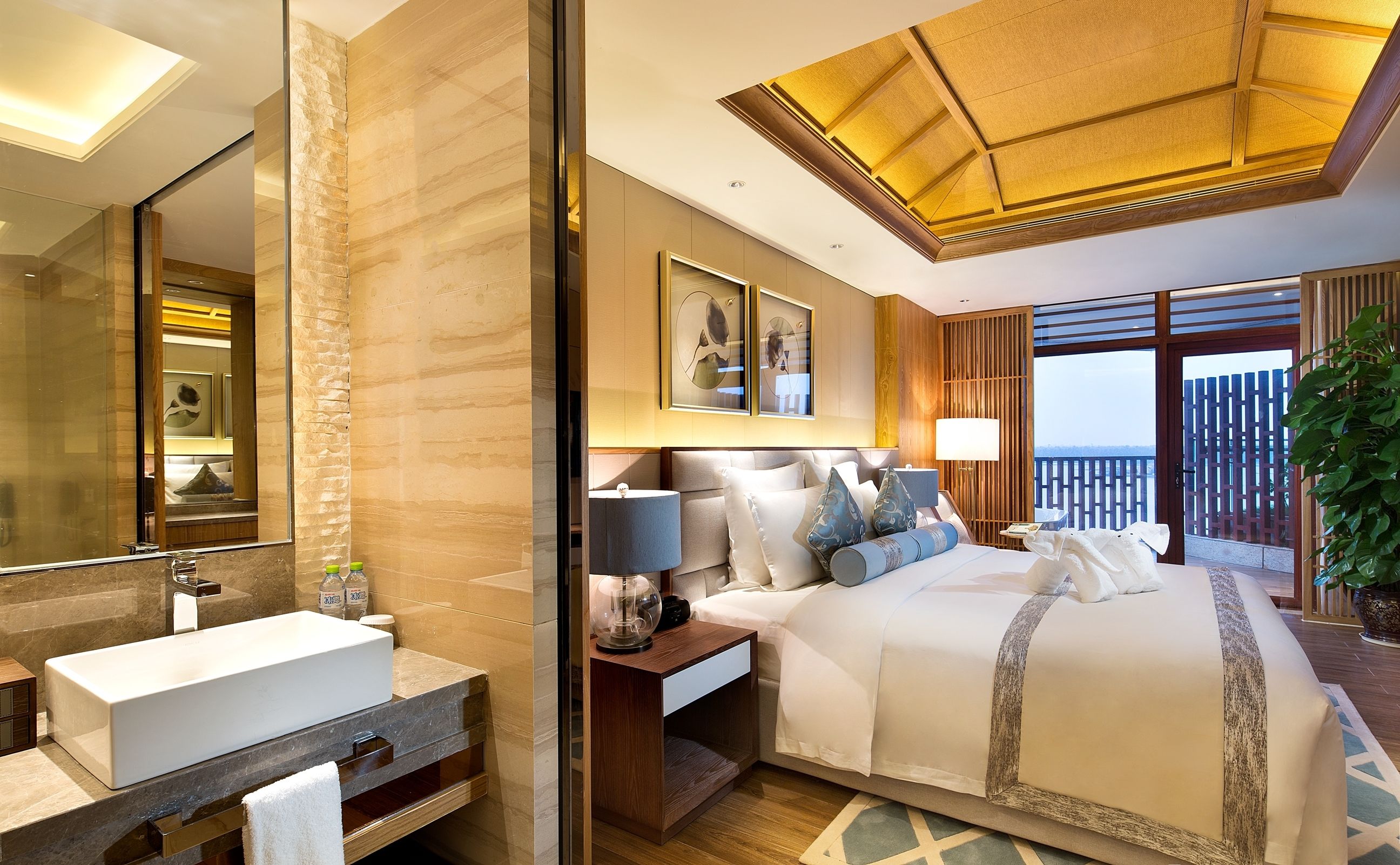 A modern hotel room with a large bed, a bathroom with a sink and mirror, and a balcony with a view.
