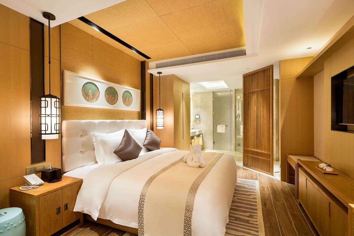 A hotel room with a large bed, bedside table, and a mirror.