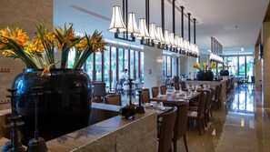 En moderne hotellobby med en lang receptionsdisk, flere spiseborde og store vinduer med udsigt til det fri.