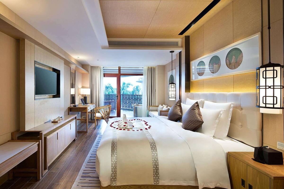 A hotel room with a large bed, a desk, a TV, and a view of the outdoors.