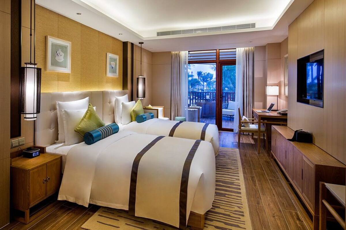 A hotel room with two beds, a desk, a TV, and a view of the outdoors.