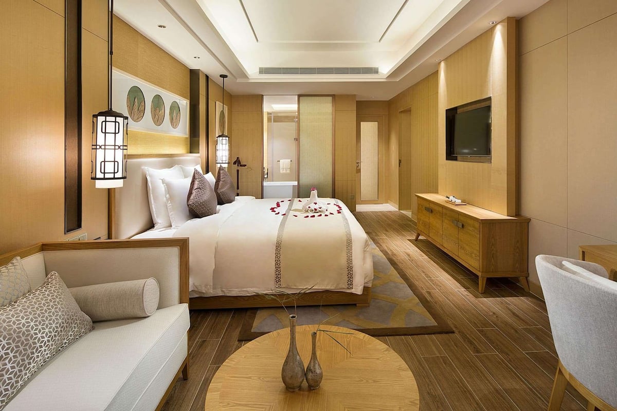 A modern hotel room with a large bed, a sofa, a TV, and a wooden cabinet.