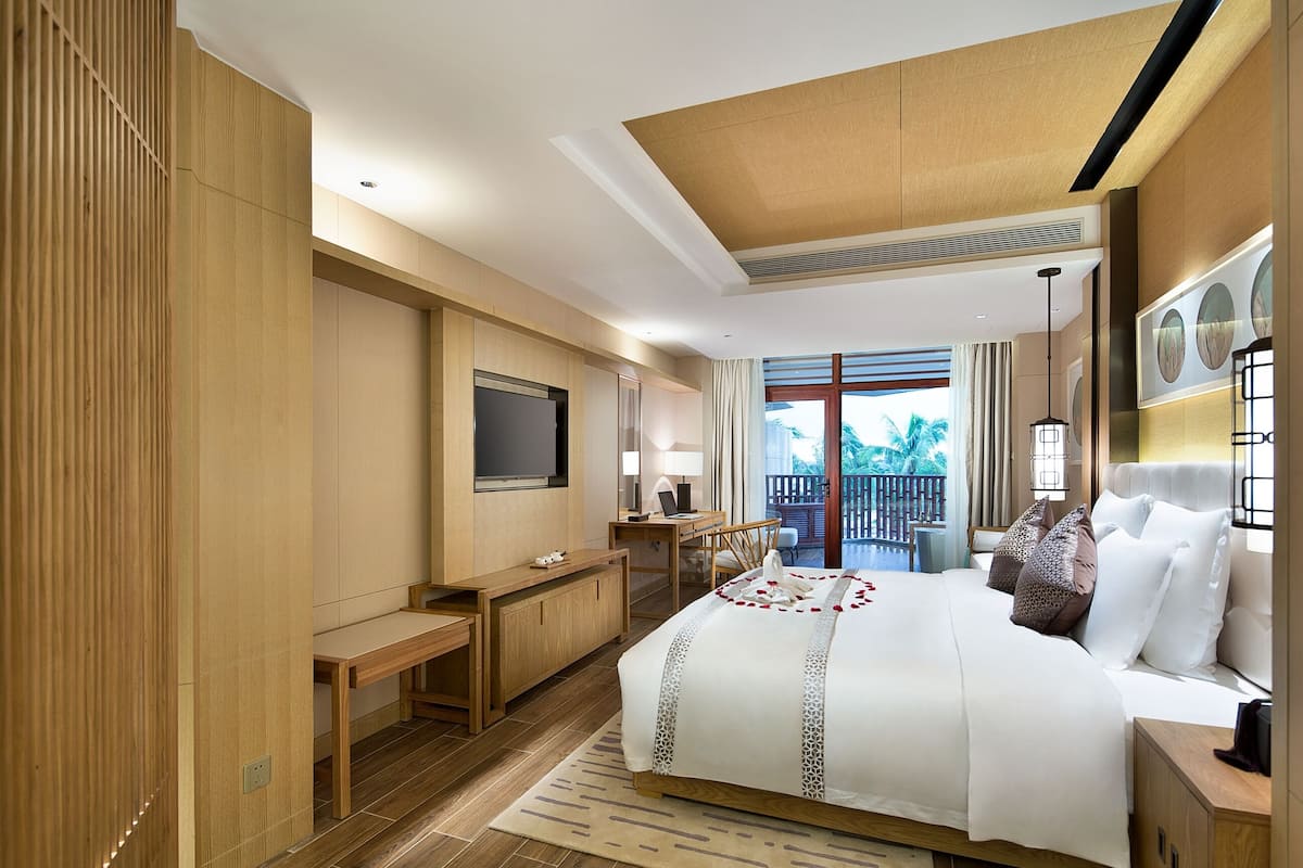 A modern hotel room with a large bed, a desk, and a balcony with a view.