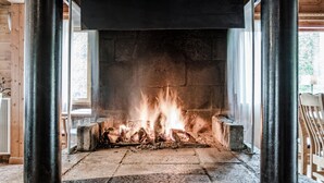 A fireplace with burning logs, a stone hearth, and a view of the outdoors through a window. - Storsätra Fjällhotell (Idre)