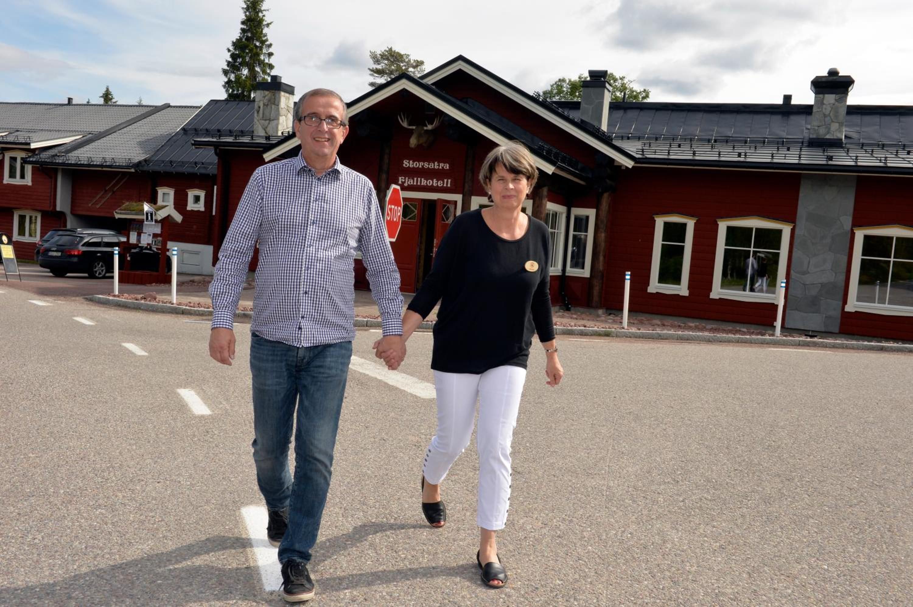 Two people walking on a street in front of a building with a sign that reads 'Storsatran Fjallhotel.'