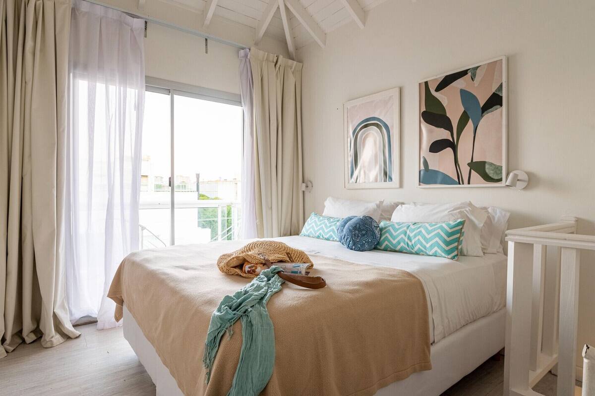 Un dormitorio con una cama, cortinas, un ventanal y dos obras de arte en la pared.