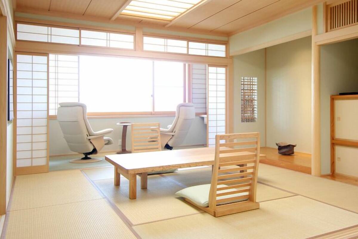 A traditional Japanese room with tatami flooring, a low table, two chairs, and a shoji screen.