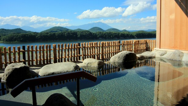A clear pool with wooden fencing and rocks, a wooden building, and a view of mountains and a lake.