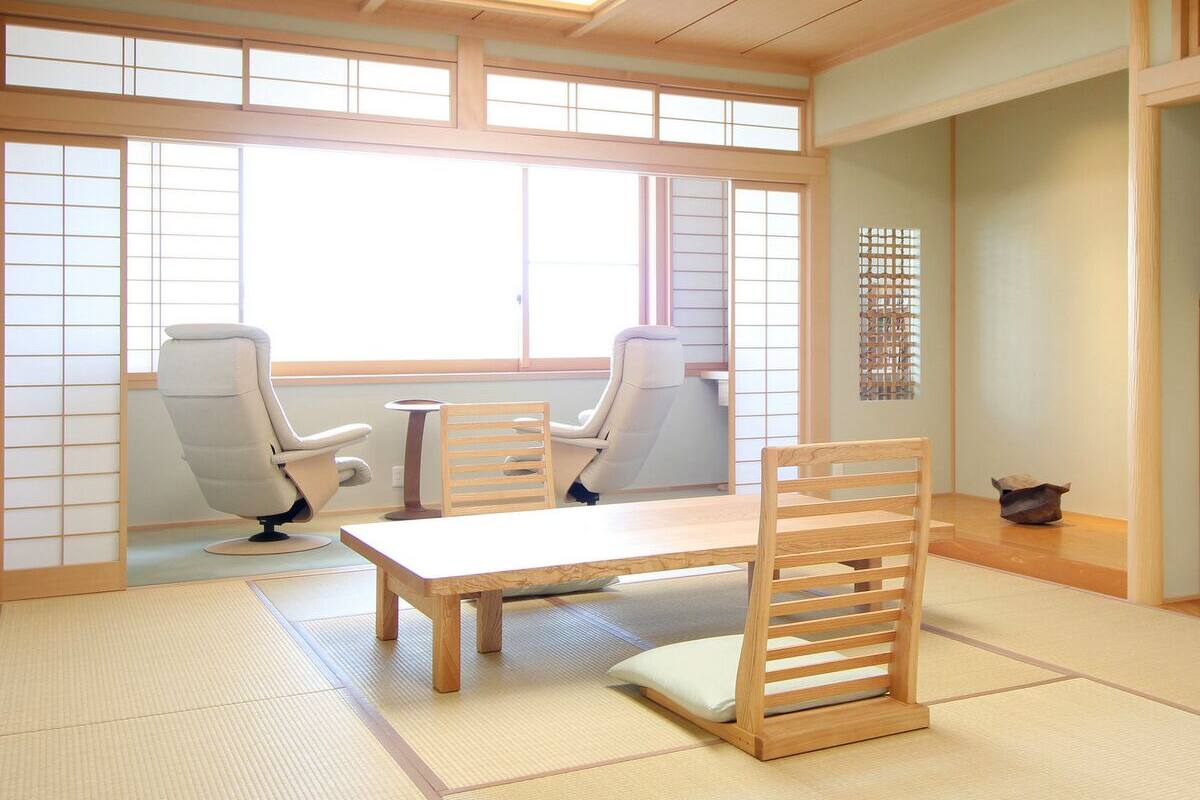 A traditional Japanese room with tatami flooring, a low table, two chairs, and sliding doors.